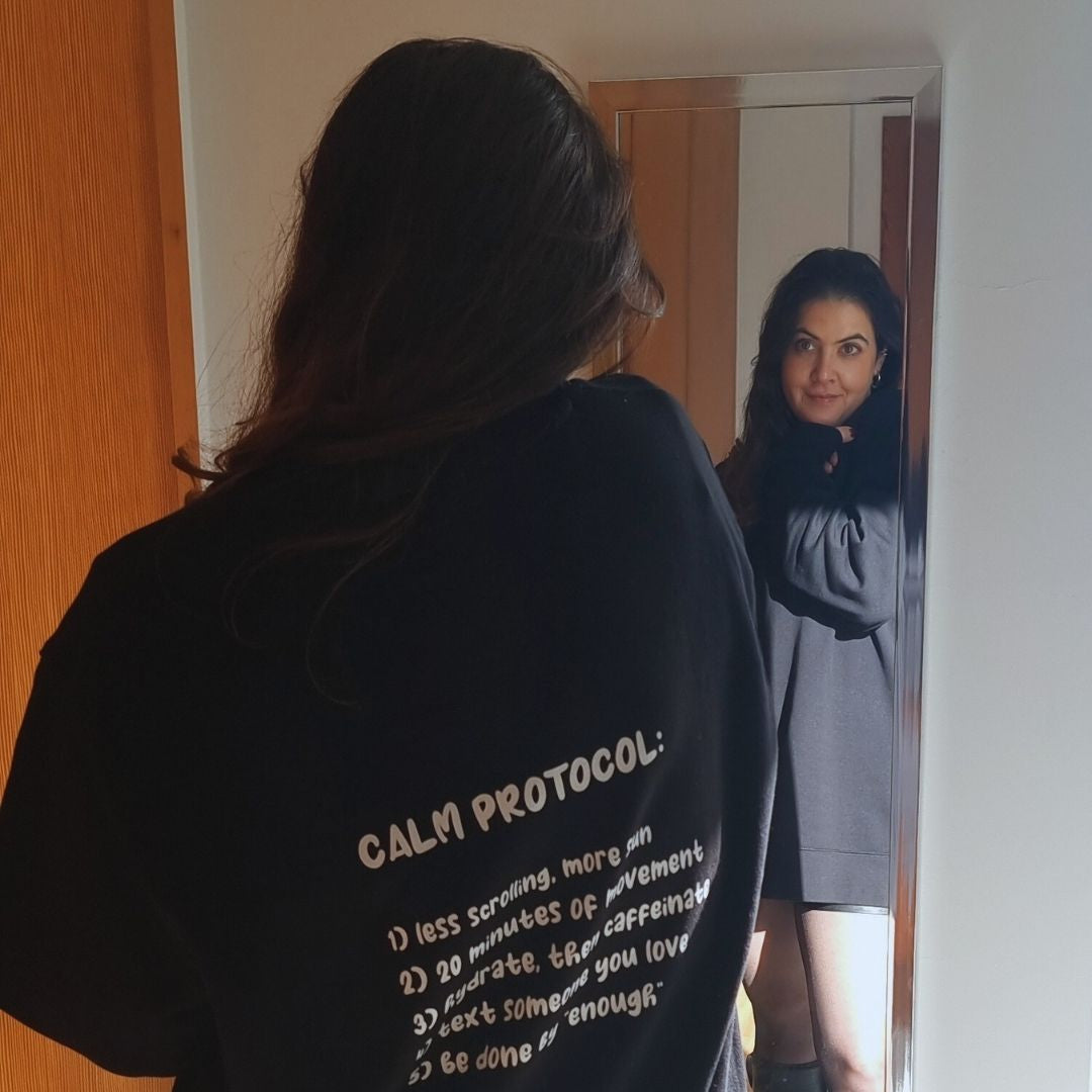 The back of a black "Calm Protocol" sweatshirt, reflected in a mirror as Rita takes the photo.
