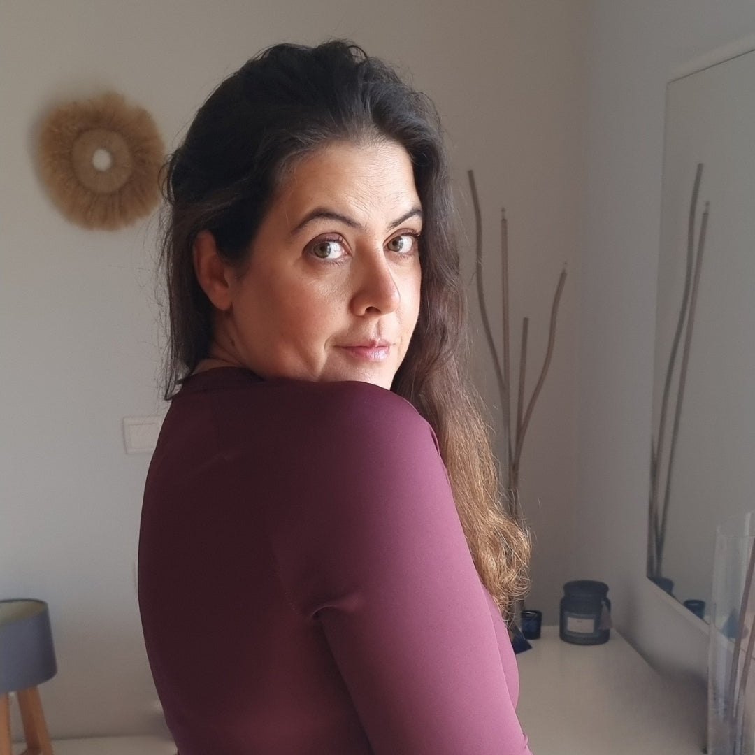 Rita Costa, founder of Aurora Soulwear, looking over her shoulder in a soft maroon top.