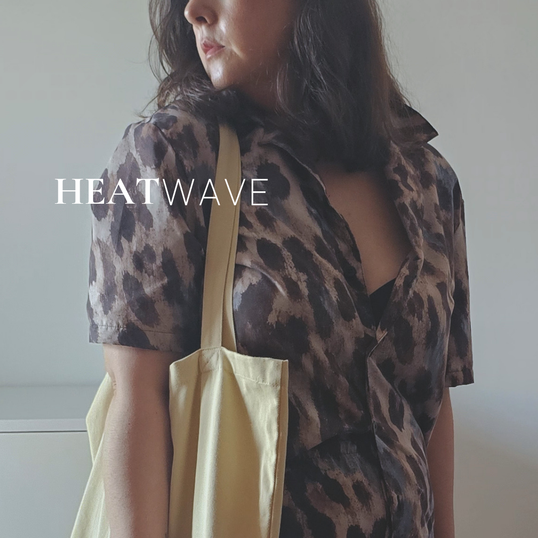A woman wearing the leopard-print Heatwave shirt, holding a pale yellow tote, a leopard scrunchie on her wrist. Aurora Soulwear Heatwave collection.